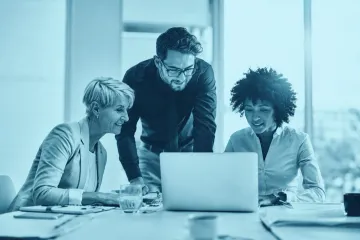 Colleagues gathered around a laptop in a meeting room, reviewing a project together